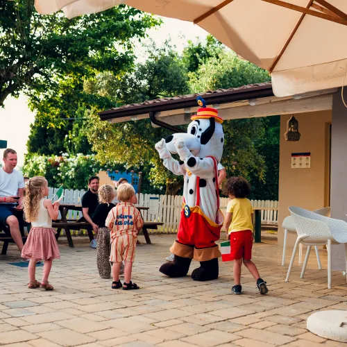 Kids smiling at a costumed character outside under a sunny patio.