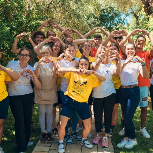 Group of people outdoors forming heart shapes with their hands, smiling.