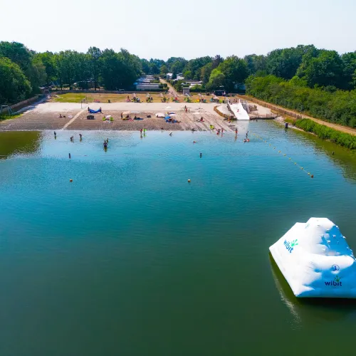 Calm lake with inflatable iceberg and sandy beach surrounded by trees.