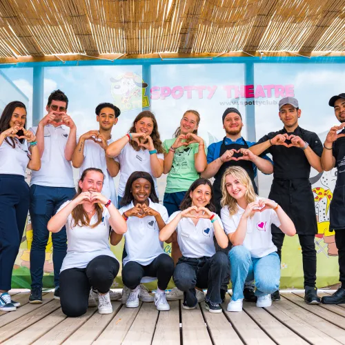 Group of people making heart shapes with hands, smiling outdoors.