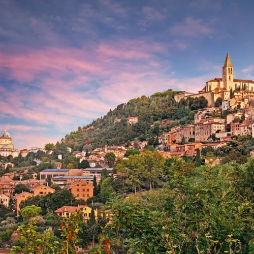 Hilltop town with sunset sky, lush greenery, and rustic buildings.
