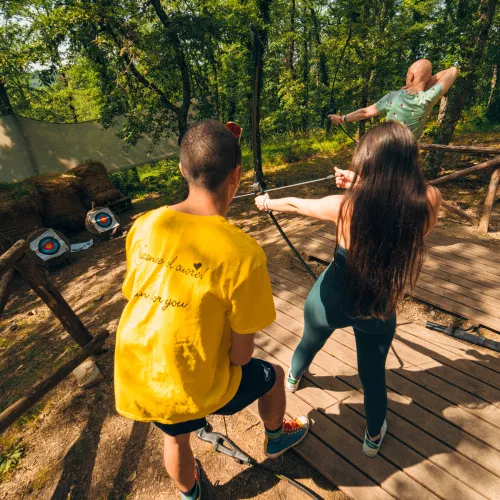 People practicing archery in a sunny forest setting.