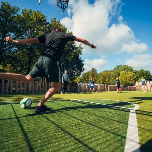 Man kicking soccer ball on outdoor field, blue sky above.
