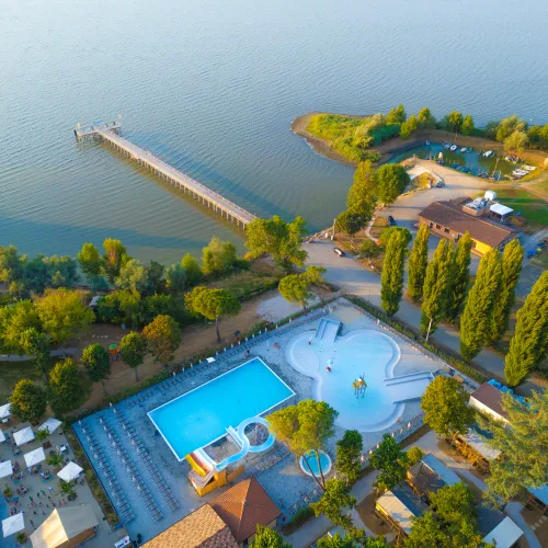 Aerial view of trasimeno lakeside resort with pool, pier, and trees.