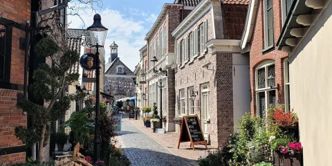 Narrow cobblestone street lined with quaint brick buildings under a clear blue sky.