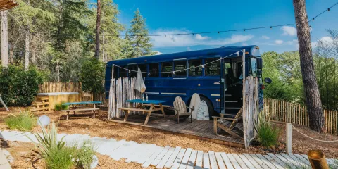Blue bus converted into a cozy outdoor seating area in a forest setting.