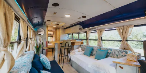 Converted bus interior with blue accents, couches, and a small dining area.