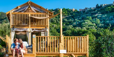 Air lodge with people seated, set against a green hillside under a blue sky.