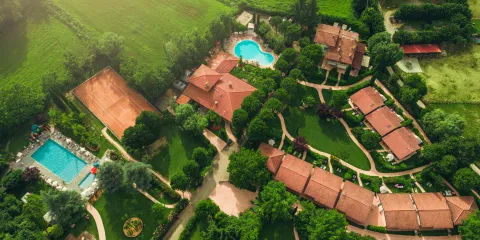 Aerial view of resort with two pools, surrounded by green fields and trees.