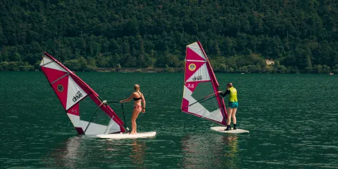 Windsurfers on a lake with forested hills in the background.