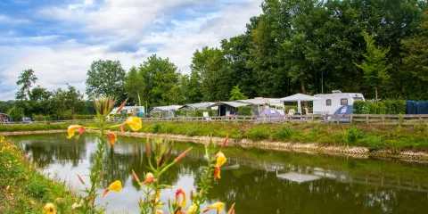 Riverside campground with tents and caravans under a cloudy sky.