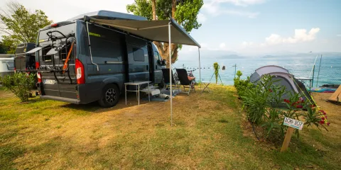 Campervan and tent on grassy lakeside campsite under clear blue sky.