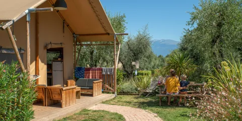 Tent with patio in sunny garden, group seated at table, distant mountains.