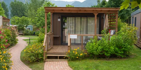 Small wooden cabin with a porch, surrounded by greenery and a winding brick path.
