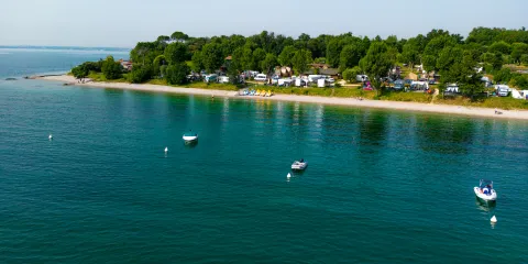 Coastal campsite with calm waters and several anchored boats.