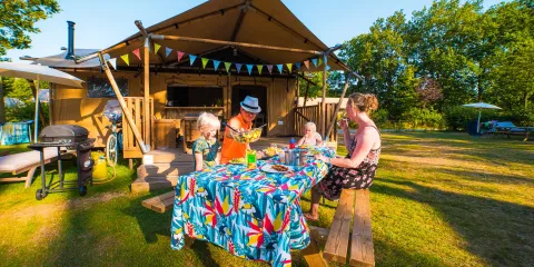 Family enjoying a picnic at a colorful table outside a wooden hut.