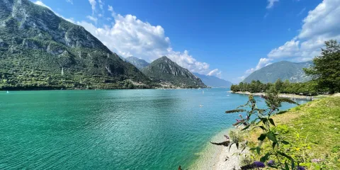 Mountainous lake landscape under a bright blue sky with fluffy clouds.