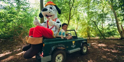 Spotty on a mini Jeep with a smiling child in a lush forest setting.