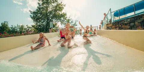 Children sliding down a water slide, smiling under a sunny sky.