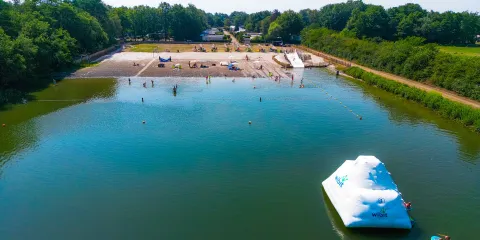 Calm lake with inflatable iceberg and sandy beach surrounded by trees.