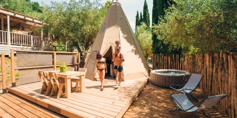 Couple exiting a tipi on a wooden deck with hot tub and chairs nearby.