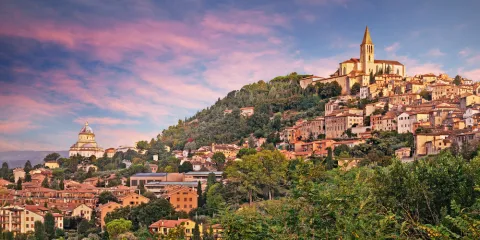 Hilltop town with sunset sky, lush greenery, and rustic buildings.