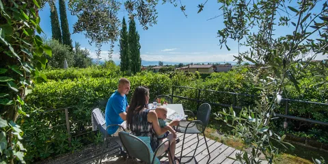 Couple sitting at garden table surrounded by lush greenery and distant view of hills.
