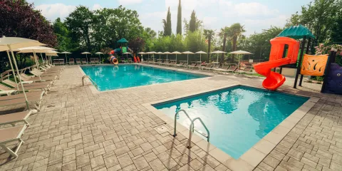 Two pools with red slides and lounge chairs under umbrellas on a sunny day.