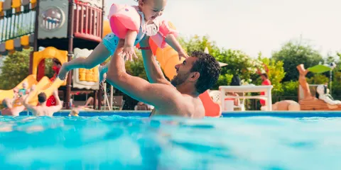 Father and child playing in a pool, surrounded by colorful playground equipment.
