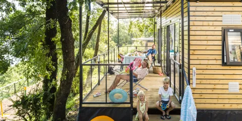 Family relaxing on a modern wooden patio in a tree-filled setting.