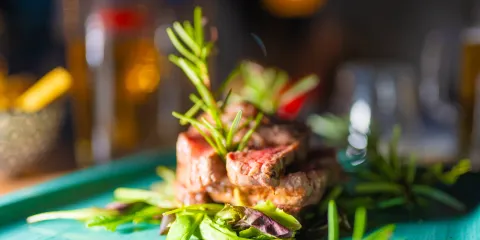 Grilled steak with rosemary on greens, served on a teal plate.