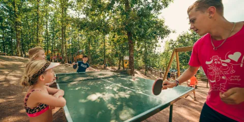 Four people playing table tennis outdoors in a sunny forest.