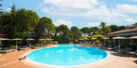 Circular pool surrounded by loungers and umbrellas, flanked by trees and a clear blue sky.