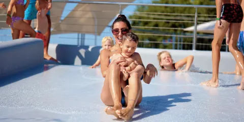 Adults and children enjoying a water slide on a sunny day.