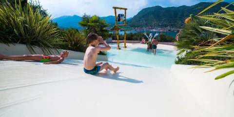 Child sliding into a pool surrounded by plants, with hills in the background.