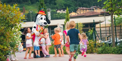 Children gather around a person in a Dalmatian costume outdoors.