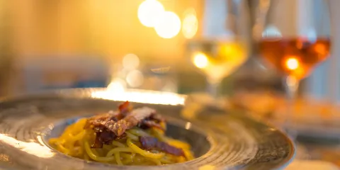 Pasta dish on a plate with two glasses of wine in a warm, softly lit setting.