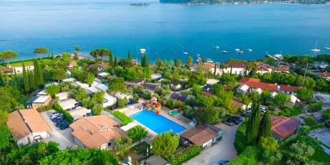 Aerial view of a lakeside resort at lake garda with pool, trees, and distant island.