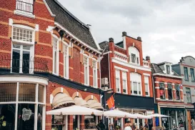 Historic street with red brick buildings, outdoor cafes, and people walking.