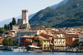 Colorful lakeside town with a castle and mountains in the background.