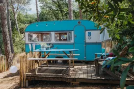 Teal caravan on a wooden deck surrounded by trees.