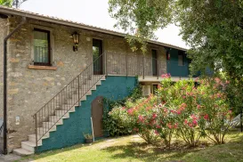 Stone building with stairs, surrounded by greenery and flowering bushes.