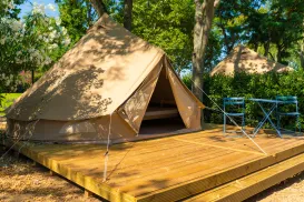 Tent on wooden platform surrounded by trees, with two blue folding chairs.