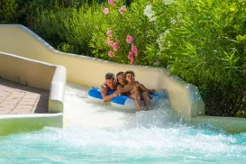Three people in an inflatable raft slide down a water slide.