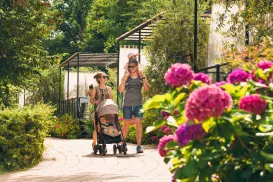Family walking with stroller on garden path, pink flowers in foreground.