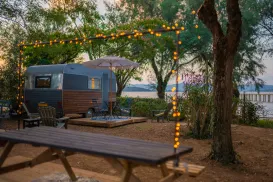 Campervan by a lake with string lights and trees at sunset.