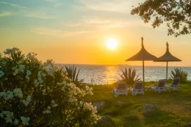 Tropical sunset over the lake with lounge chairs and parasols on the grassy shore.