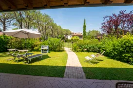 Sunny garden with lounge chairs, umbrella, and a path leading to trees and shrubs.