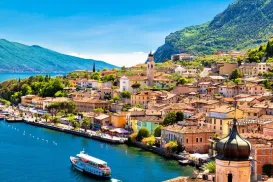 Lakefront town with colorful buildings and lush hills under a bright blue sky.
