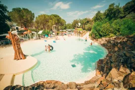 Tropical pool with people swimming, surrounded by trees and rocks.